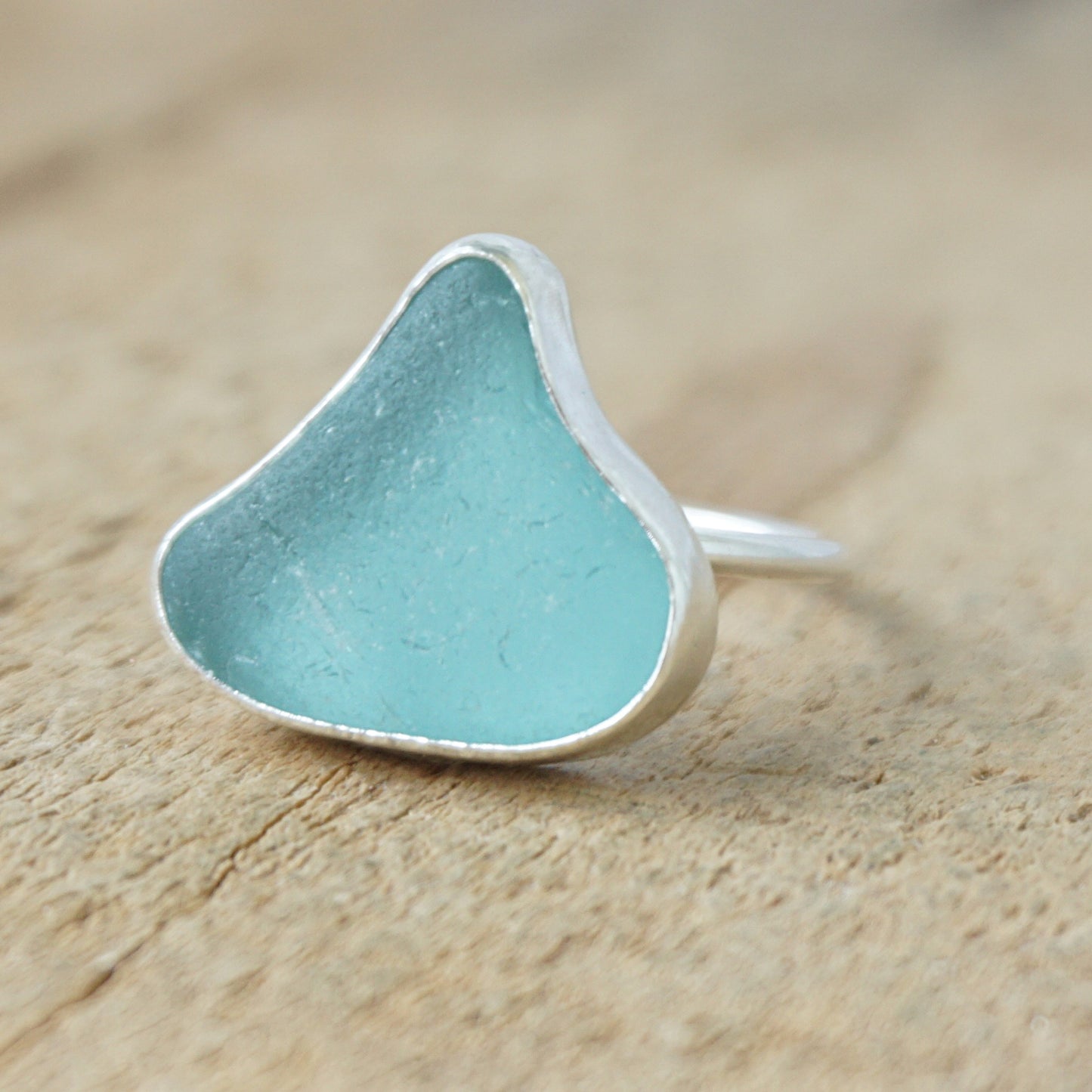 silver ring with teal sea glass on a wooden background