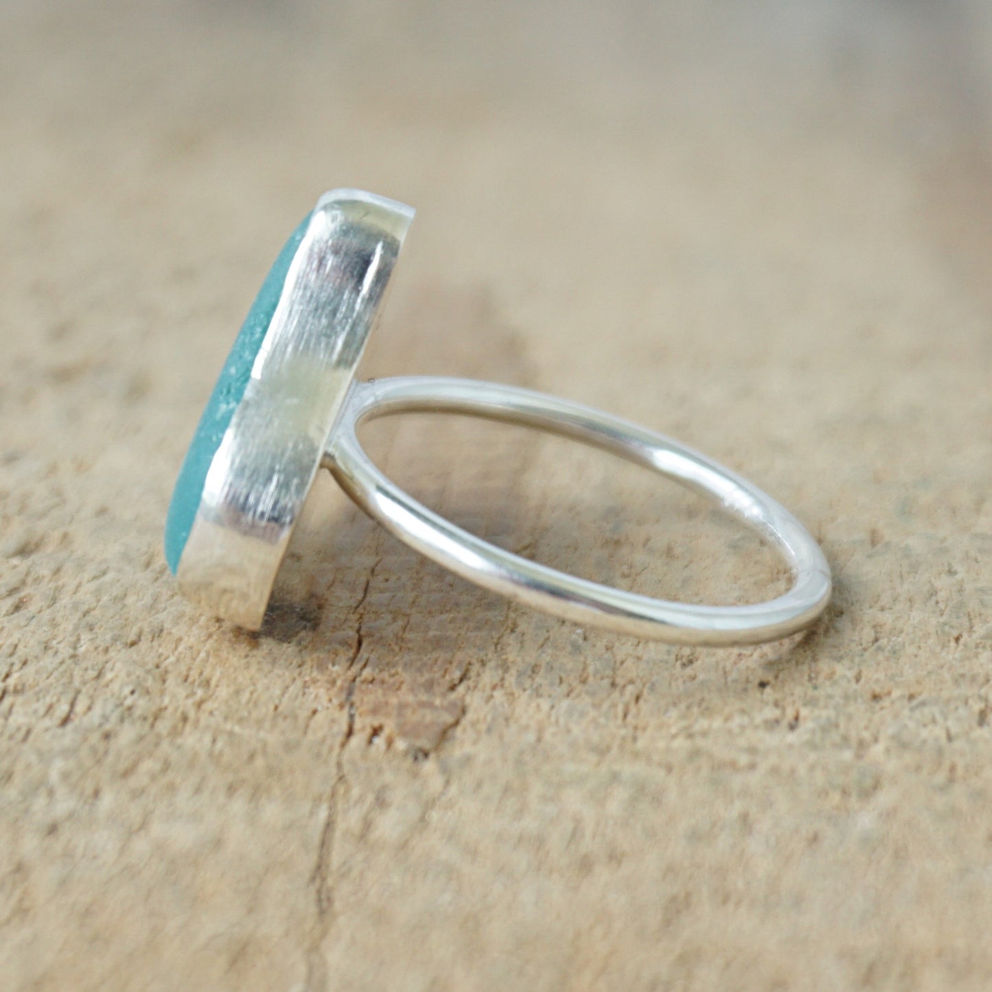 side view of a silver ring with teal sea glass on a wooden background