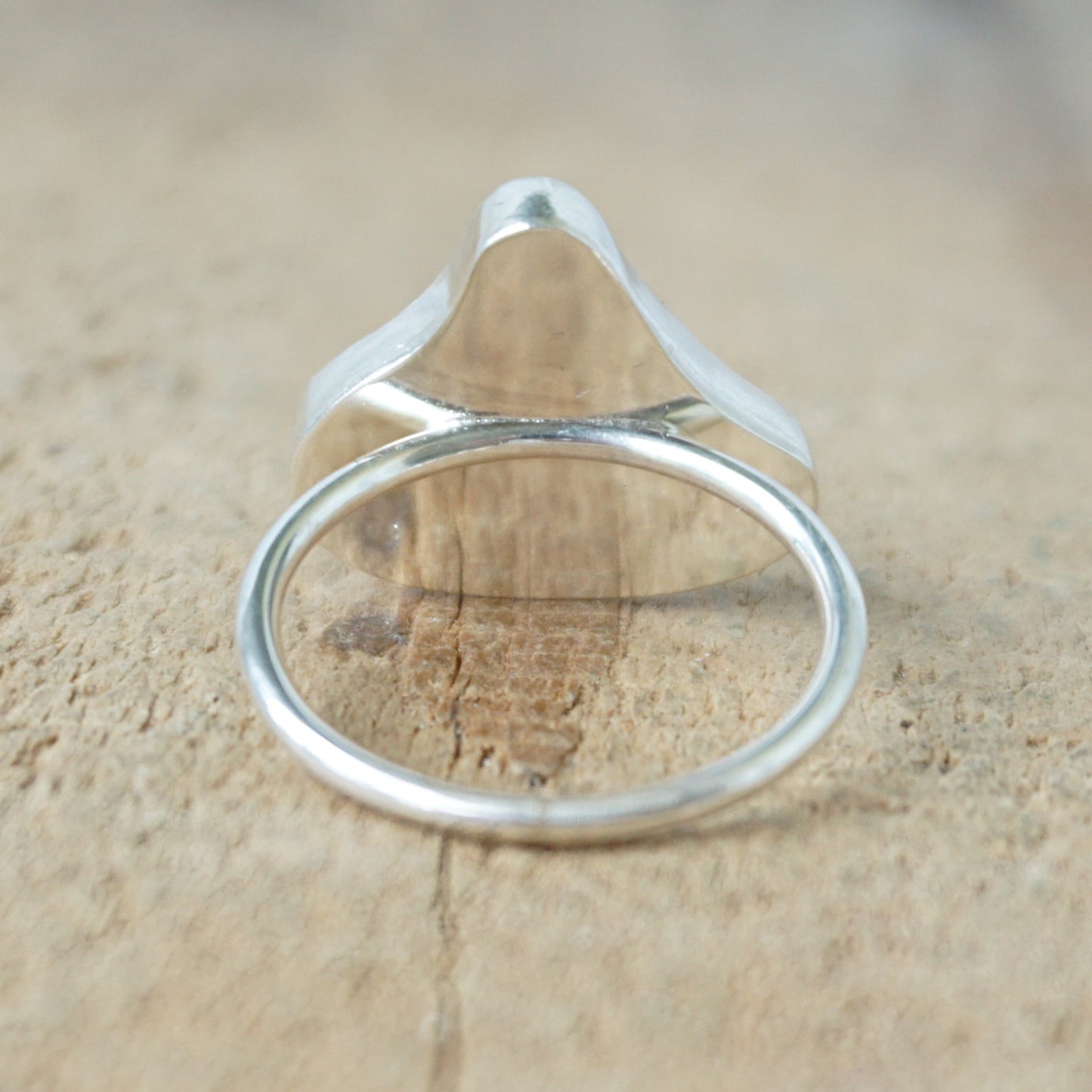 back view of a silver ring with teal sea glass on a wooden background