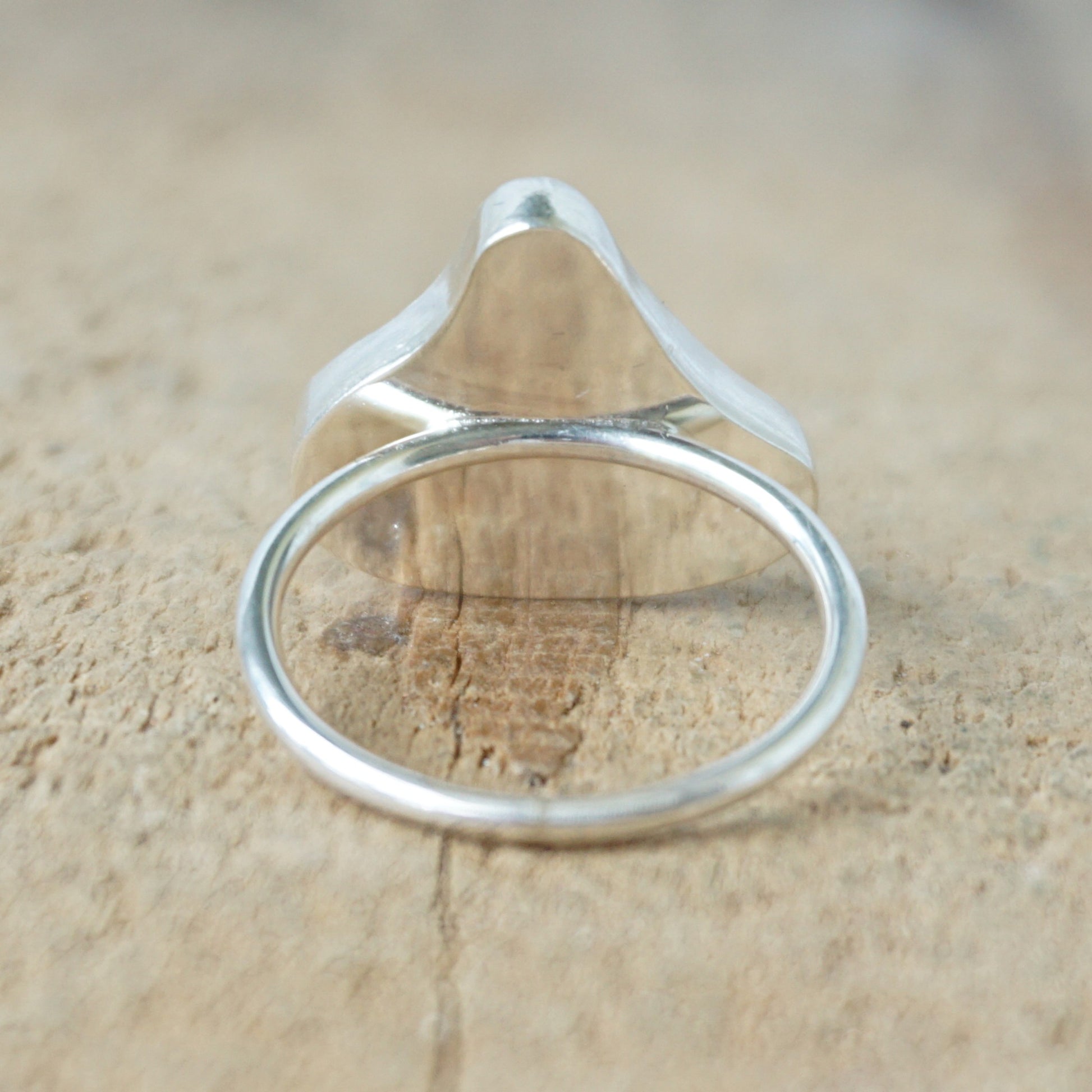 back view of a silver ring with teal sea glass on a wooden background