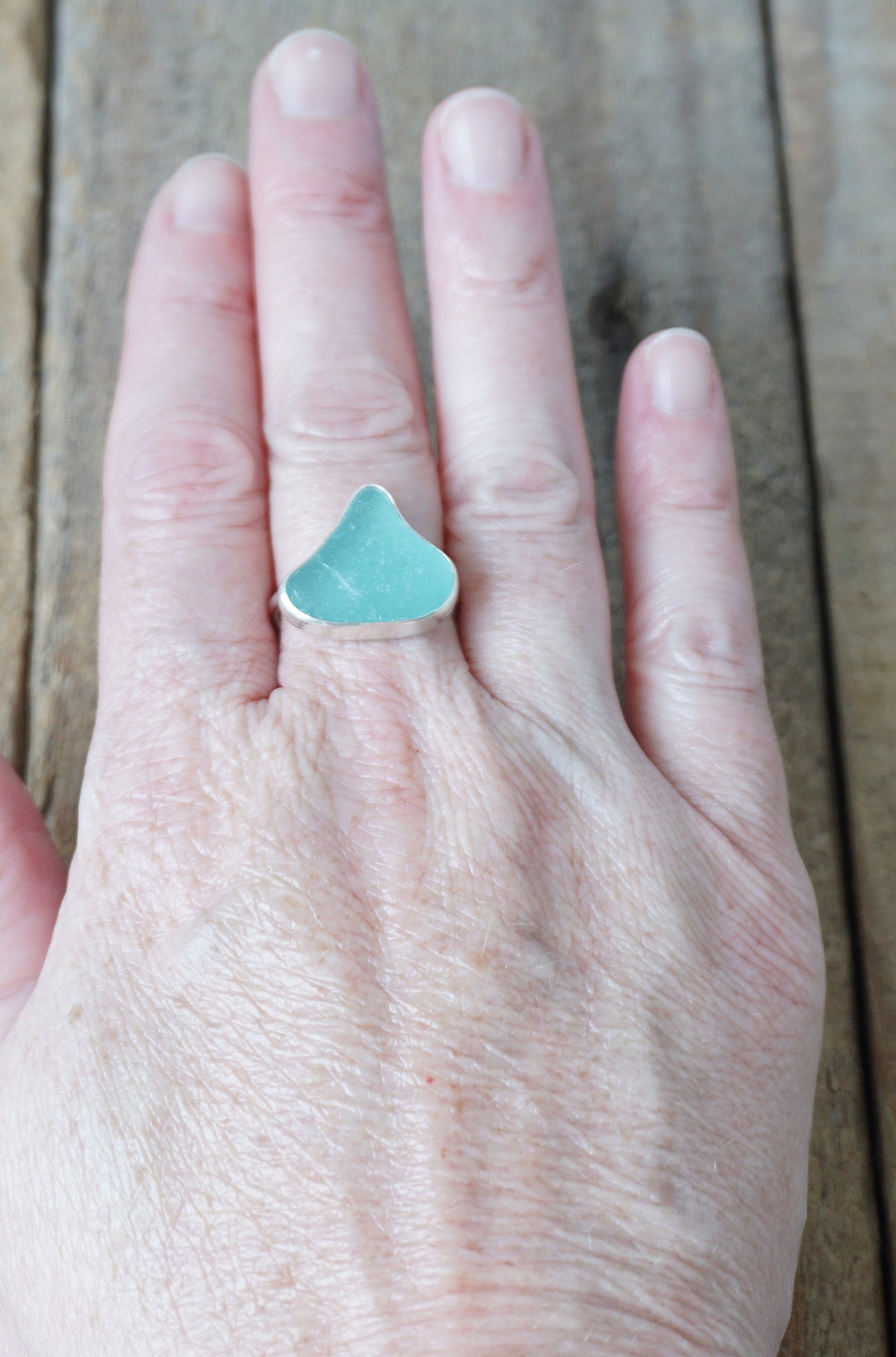 hand wearing a silver ring with teal sea glass on a wooden background