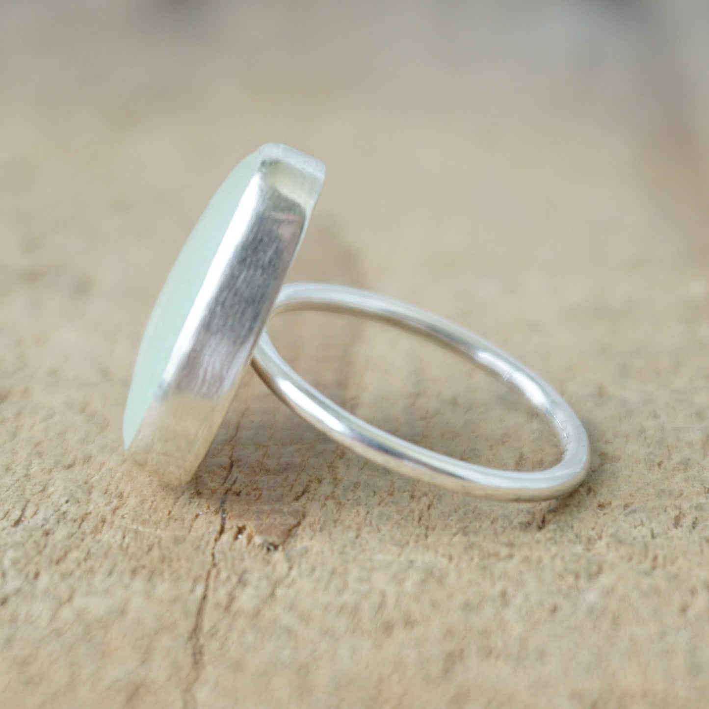 side view of a silver ring with seafoam green sea glass on a wooden background