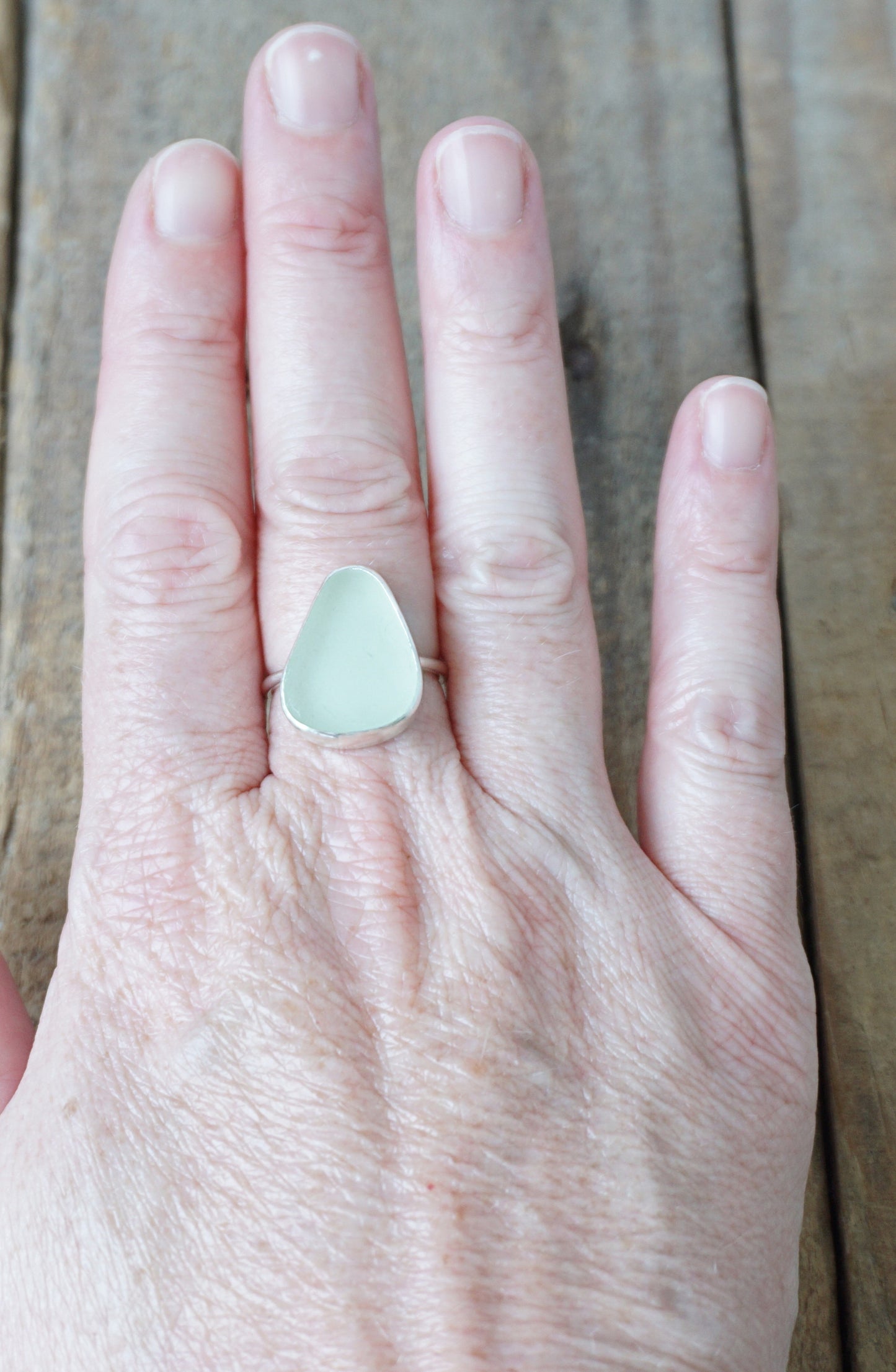 hand wearing a silver ring with seafoam green sea glass on a wooden background