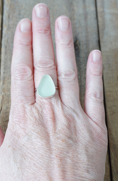 hand wearing a silver ring with seafoam green sea glass on a wooden background
