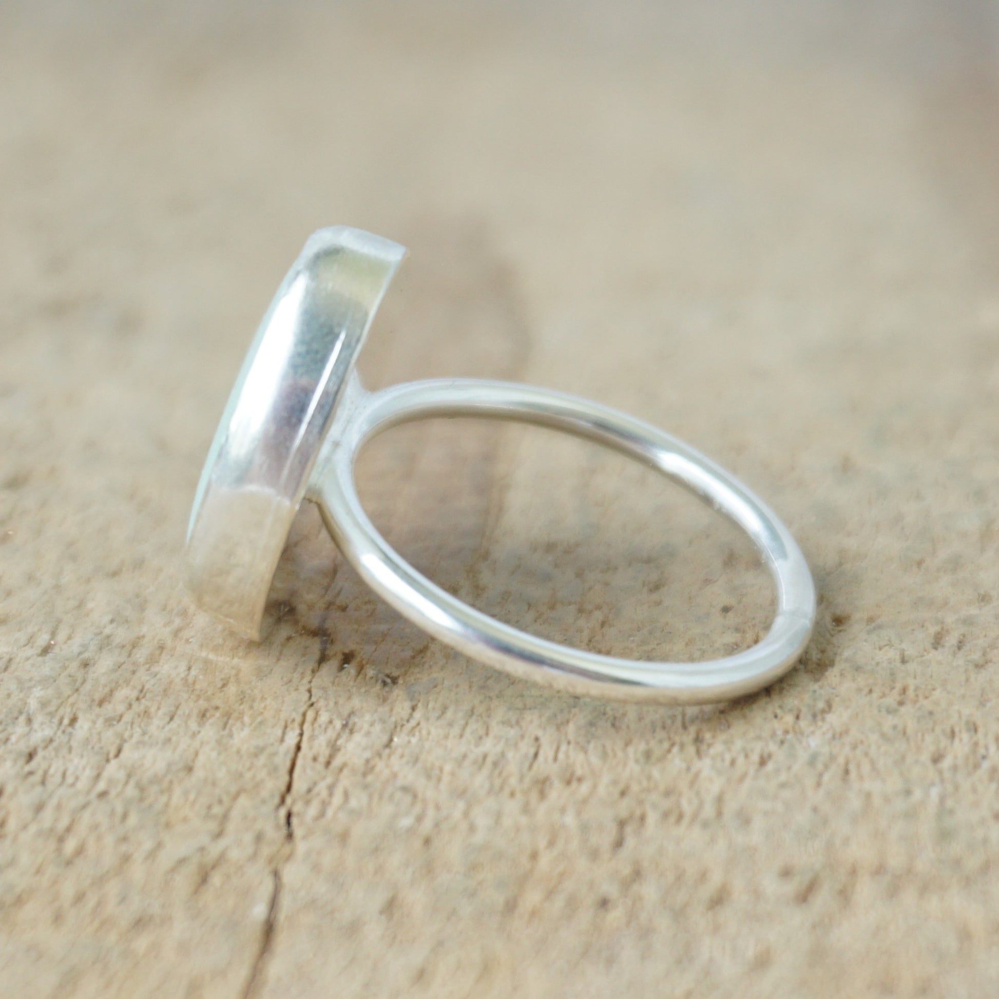 side view of a silver ring with seafoam green sea glass on a wooden background