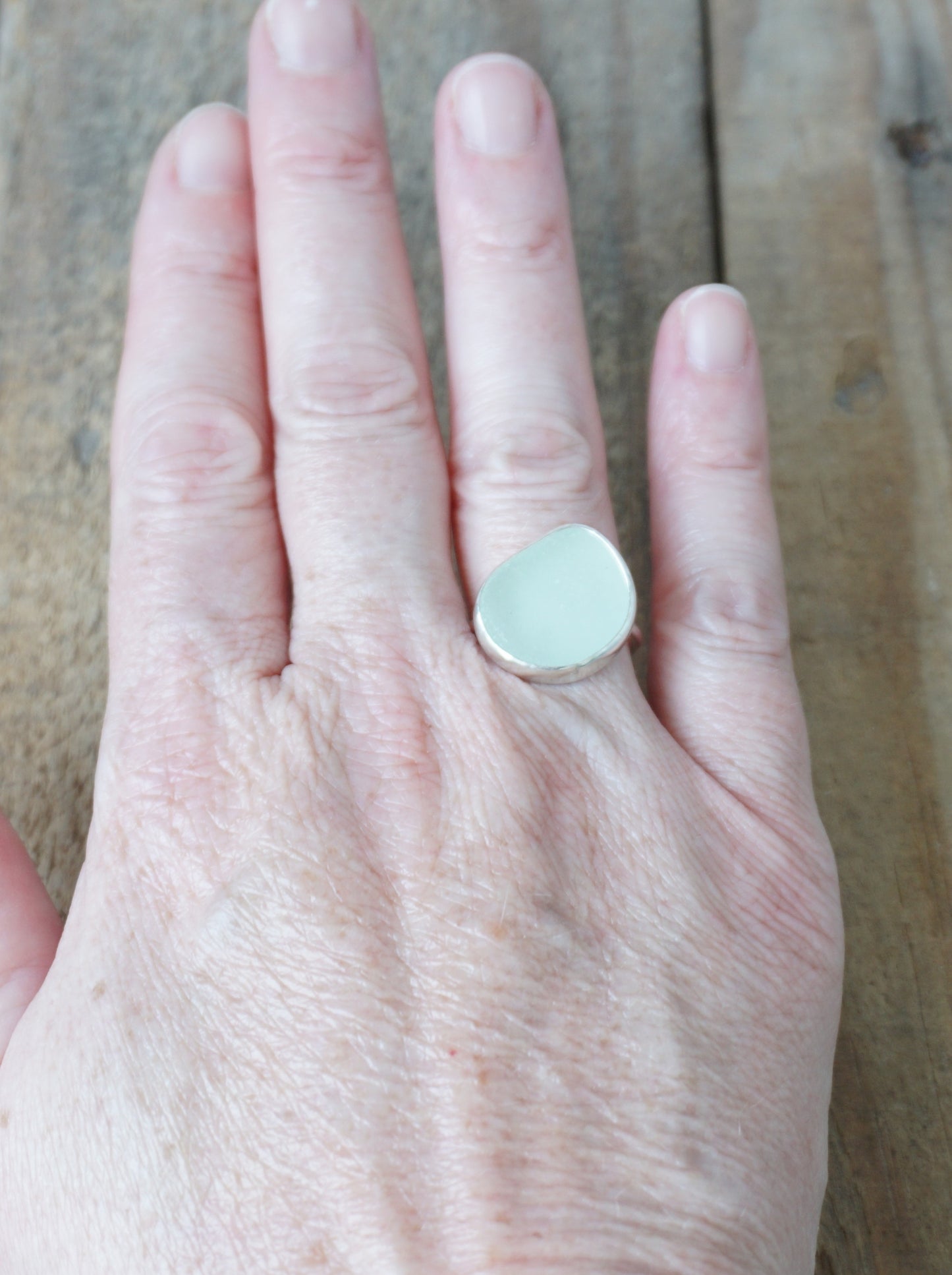 hand wearing a silver ring with seafoam green sea glass on a wooden background