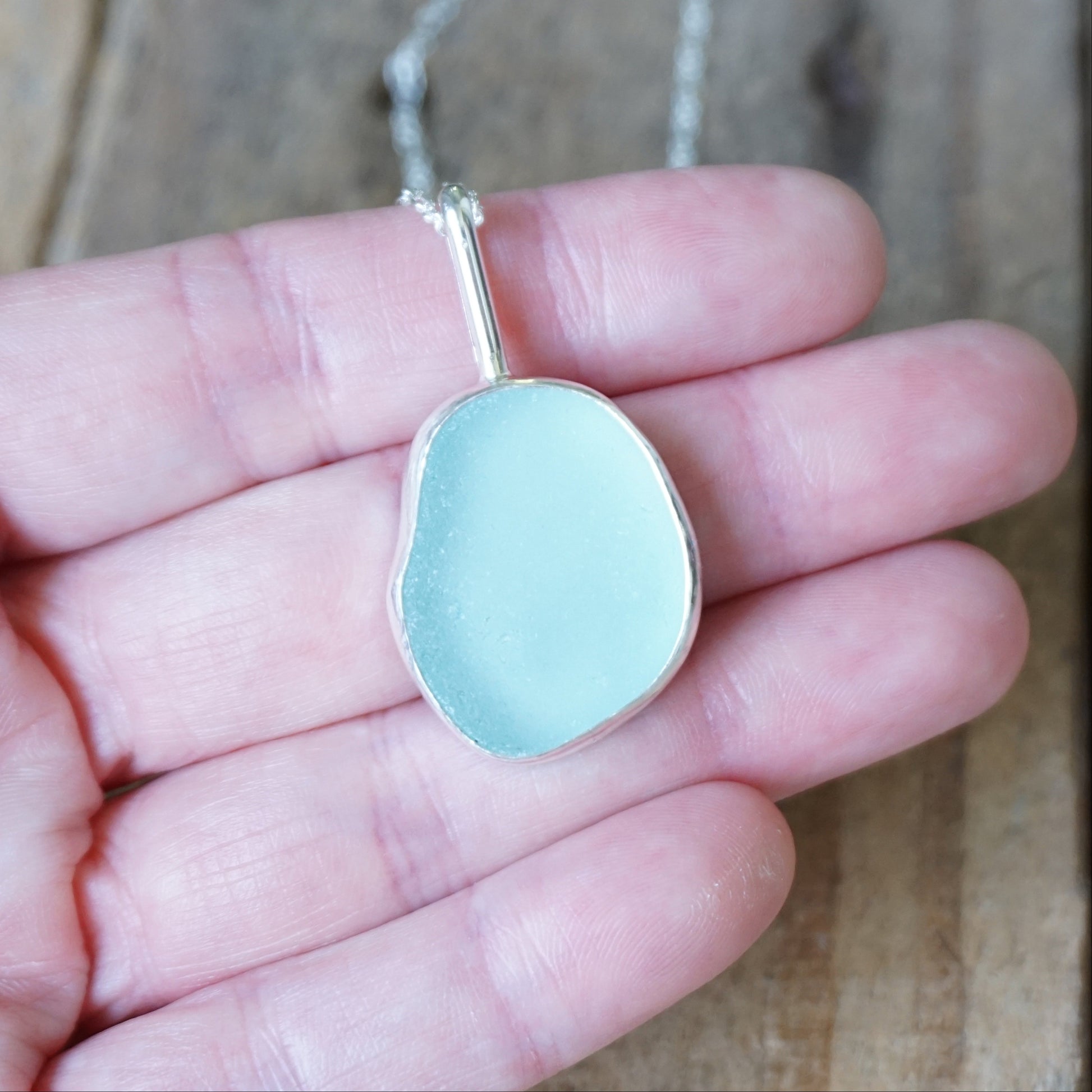 hand holding a light blue sea glass pendant on a wooden background