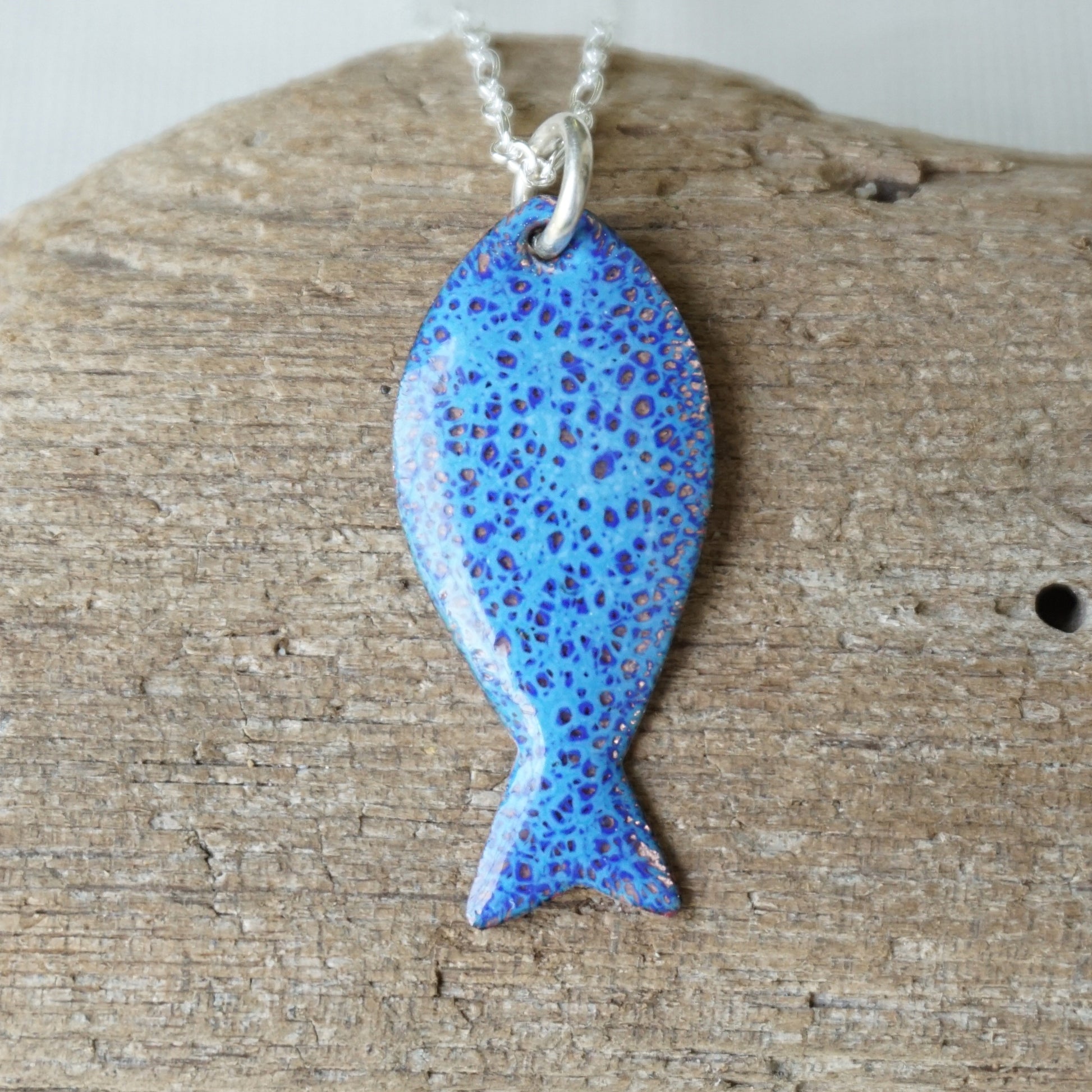 Blue speckled fish pendant on a chain against a wooden background