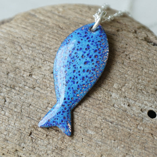 Blue speckled fish pendant on a wooden surface

