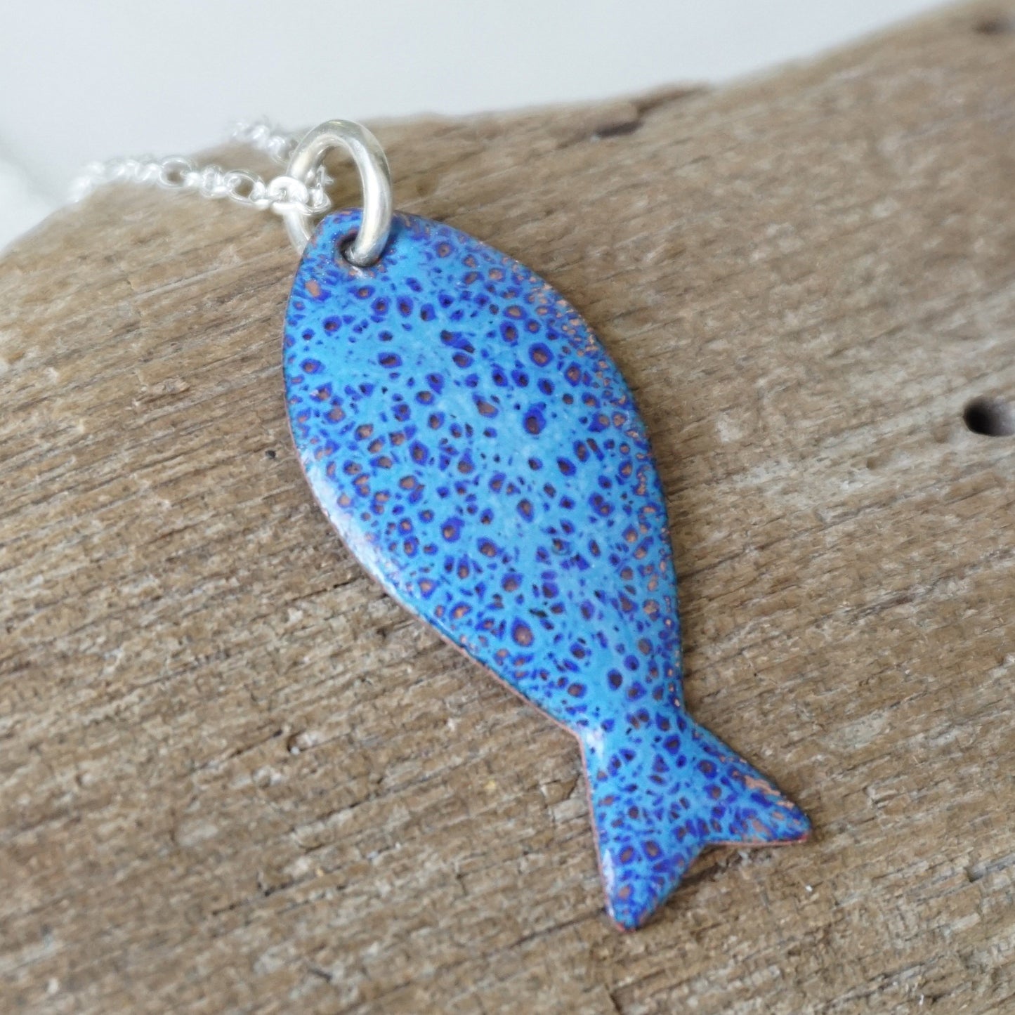 Blue speckled fish-shaped pendant on a wooden surface