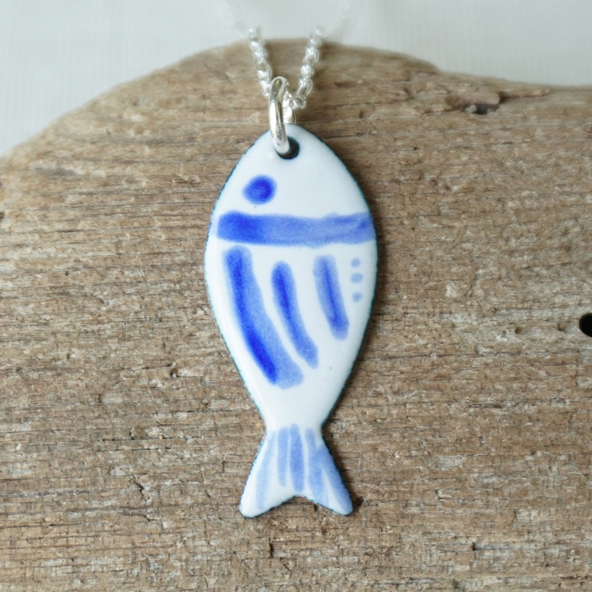 Fish-shaped pendant with blue accents on a chain, placed on a wooden surface.