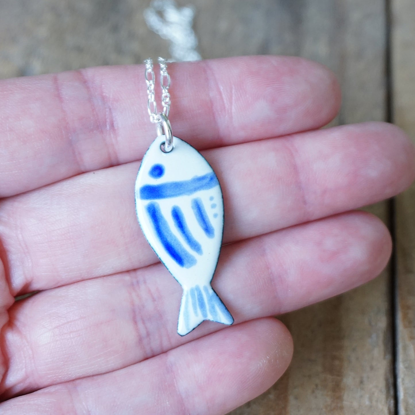 Fish-shaped pendant with blue accents on a chain held in a hand.