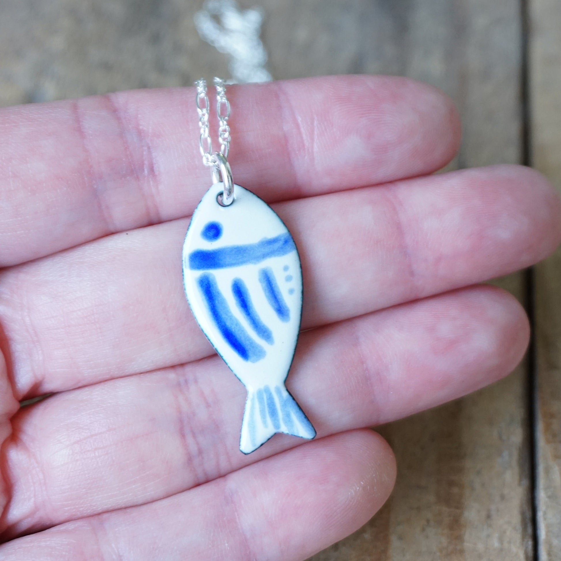 Fish-shaped pendant with blue accents on a chain held in a hand.