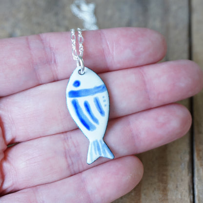 Fish-shaped pendant with blue accents on a chain held in a hand.