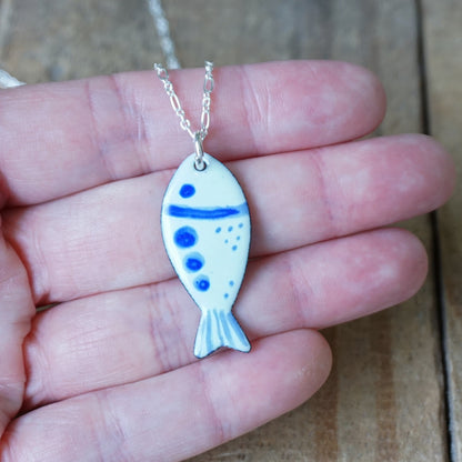 Fish-shaped pendant with blue accents on a chain held in a hand against a wooden background