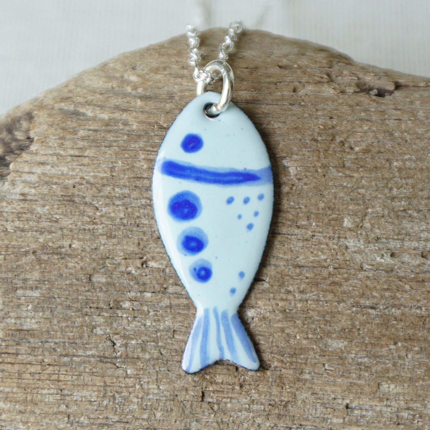 Fish-shaped pendant with blue accents on a chain, placed on wooden surface