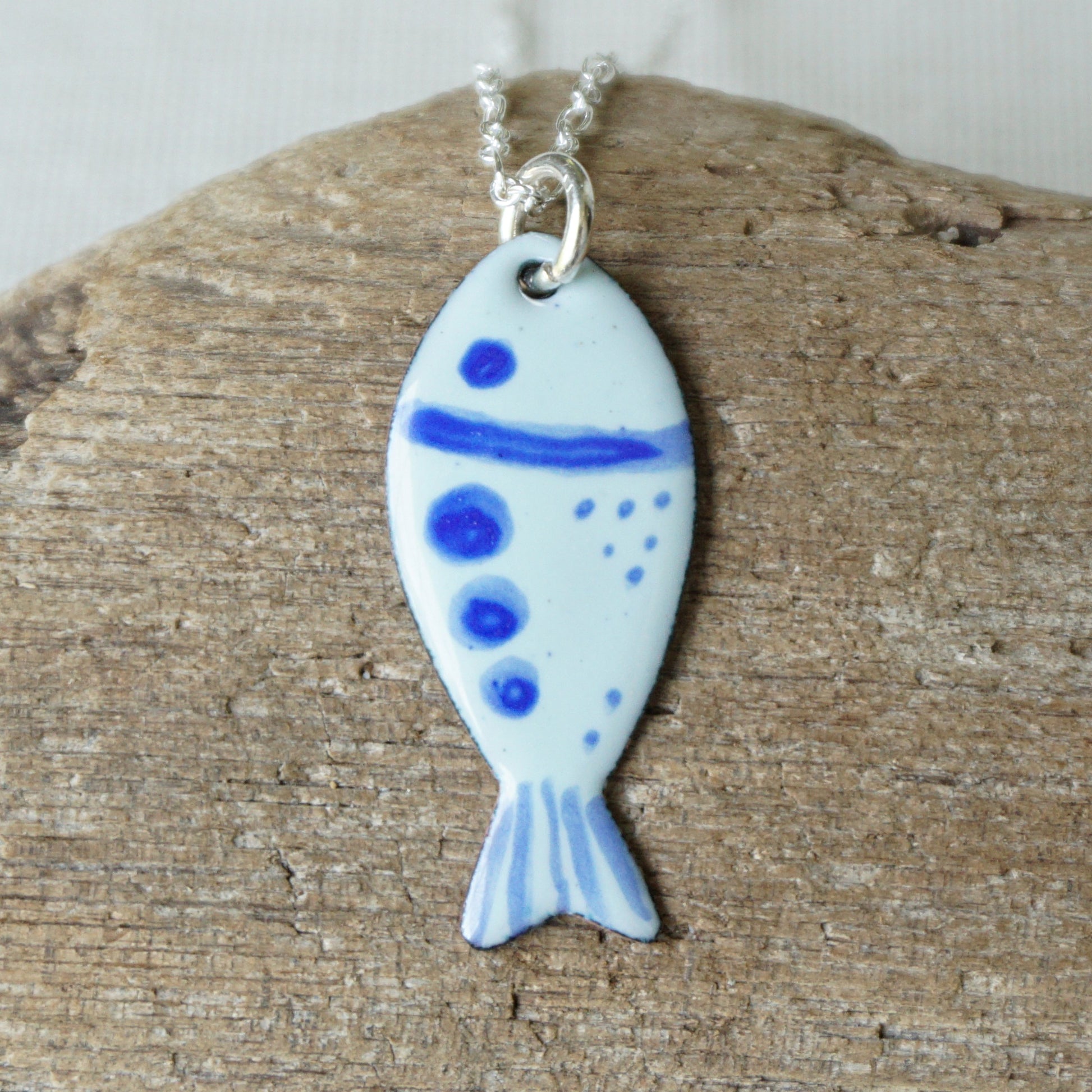 Fish-shaped pendant with blue accents on a chain, placed on wooden surface