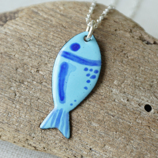 Blue fish-shaped pendant on a silver chain, placed on a wooden surface.