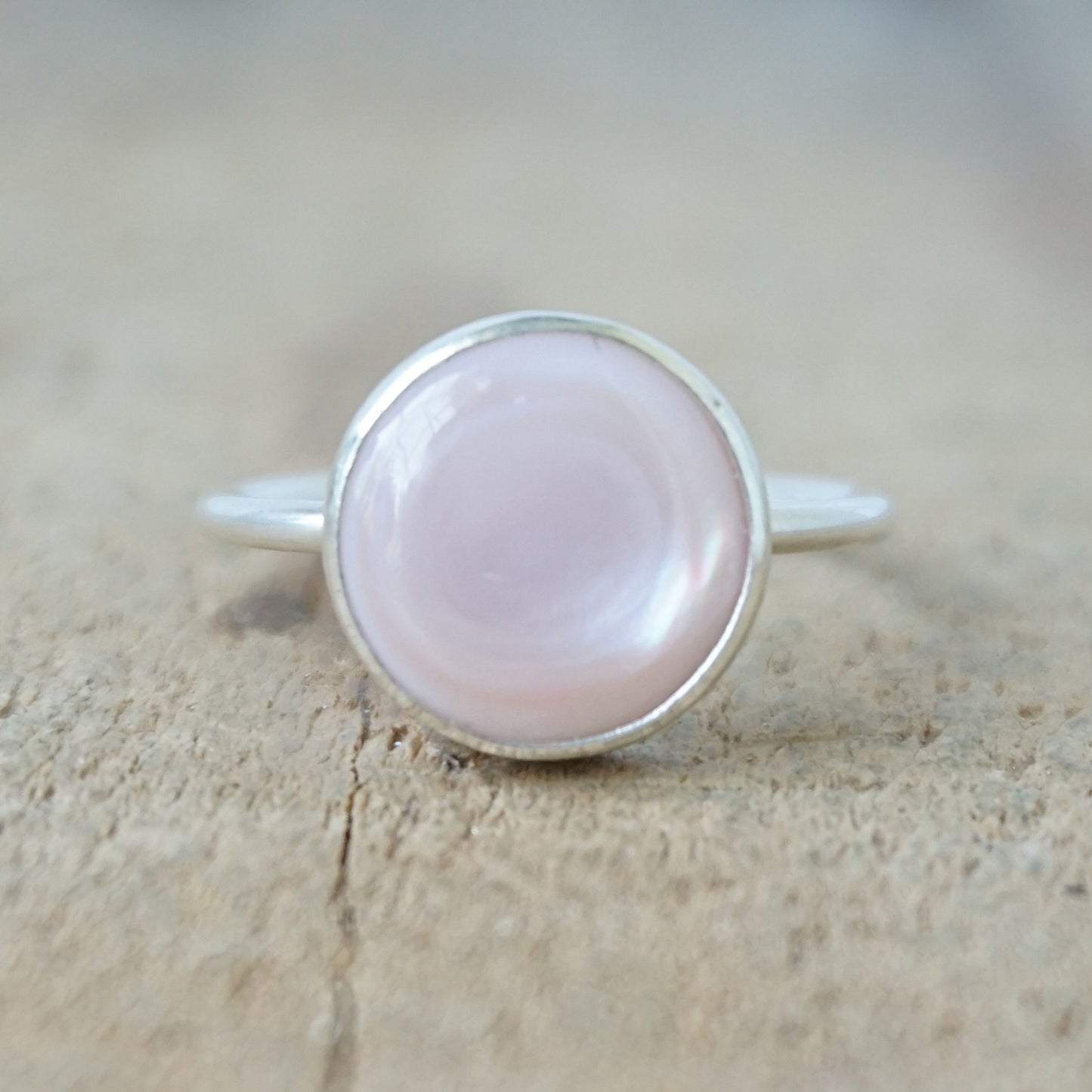 silver ring with a light pink stone on a wooden background