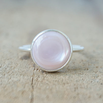 silver ring with a light pink stone on a wooden background
