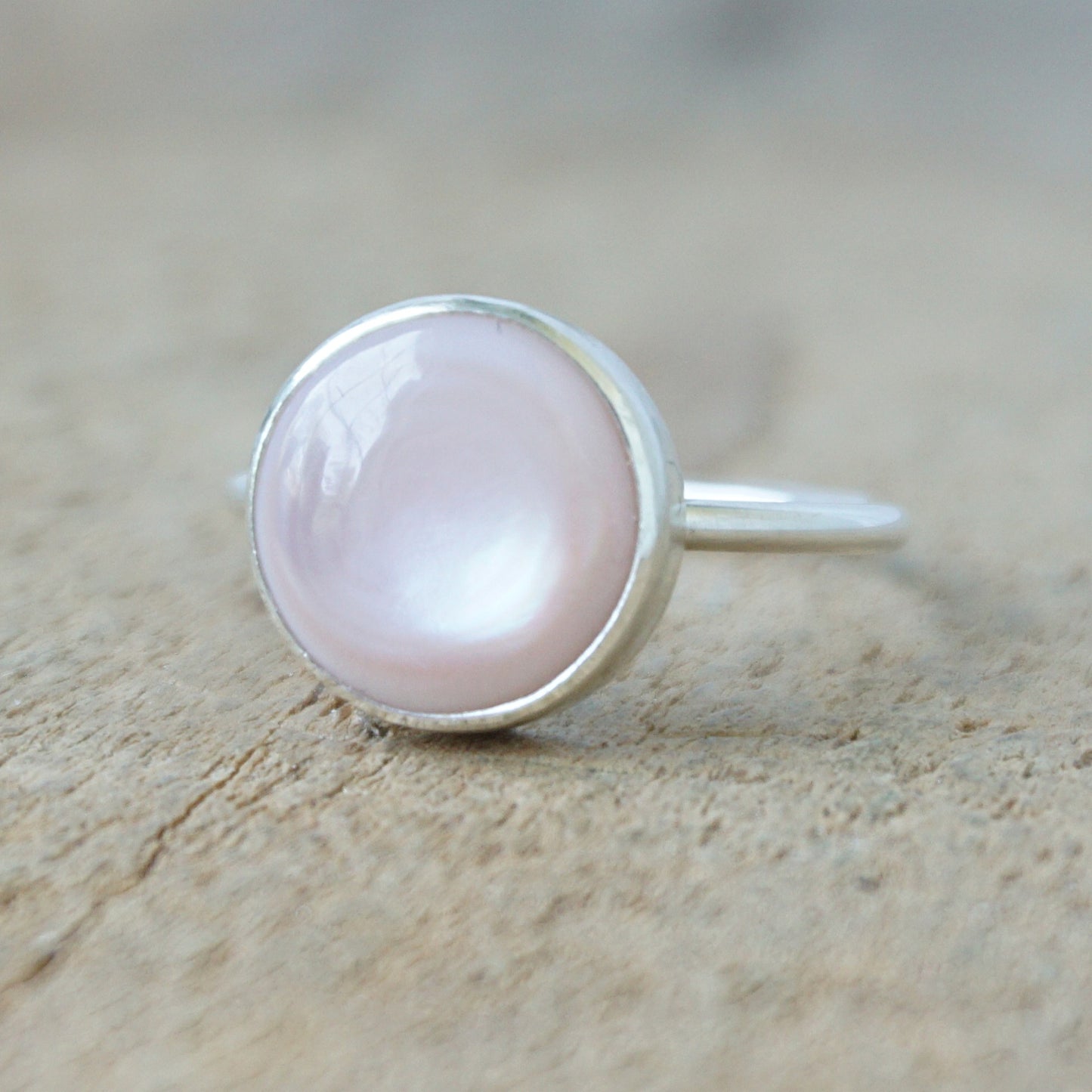 silver ring with a light pink stone on a wooden background