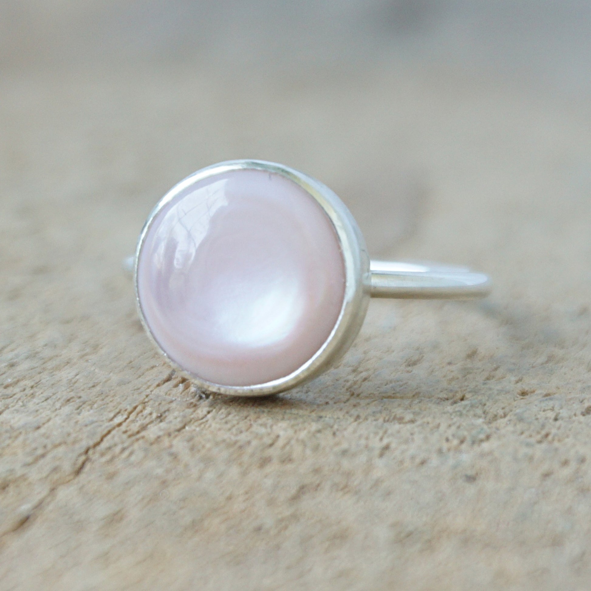 silver ring with a light pink stone on a wooden background