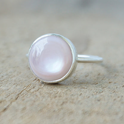 silver ring with a light pink stone on a wooden background