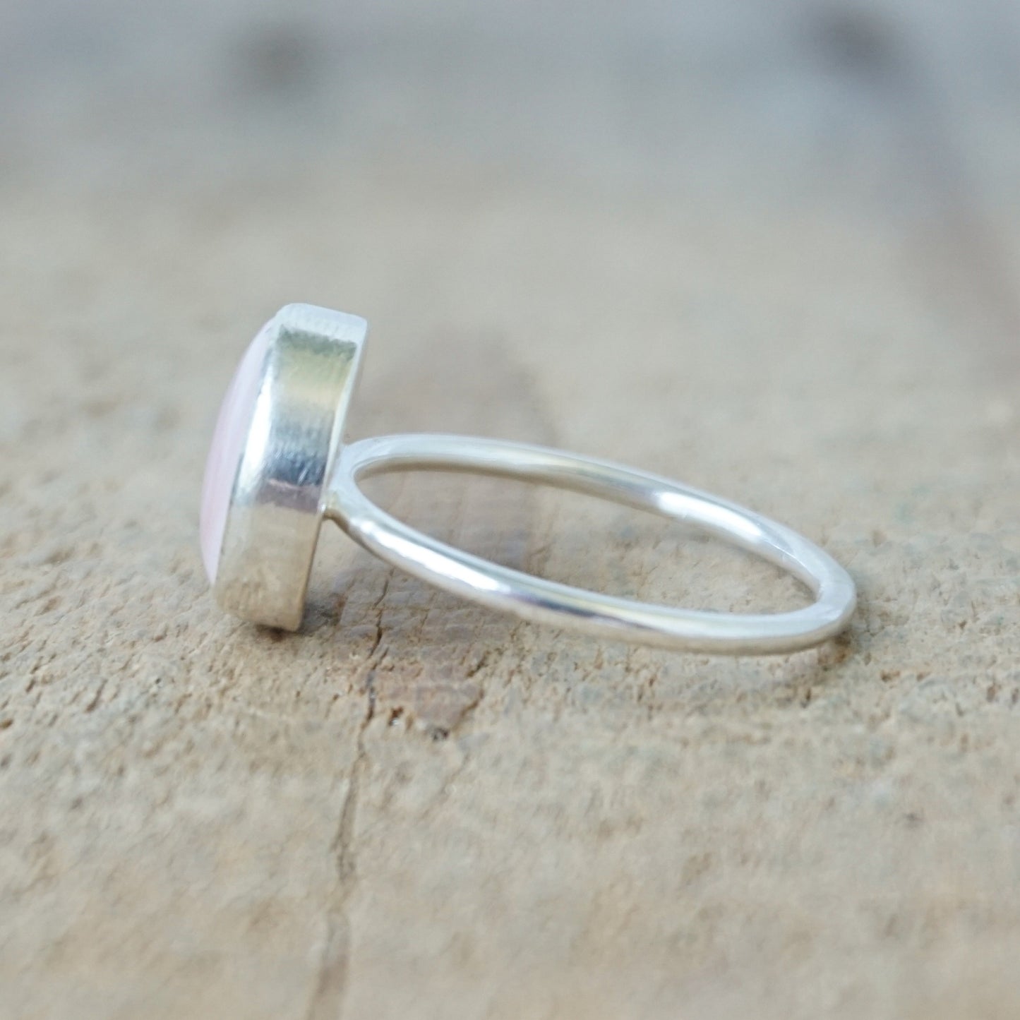 side view of a silver ring with a light pink stone on a wooden background