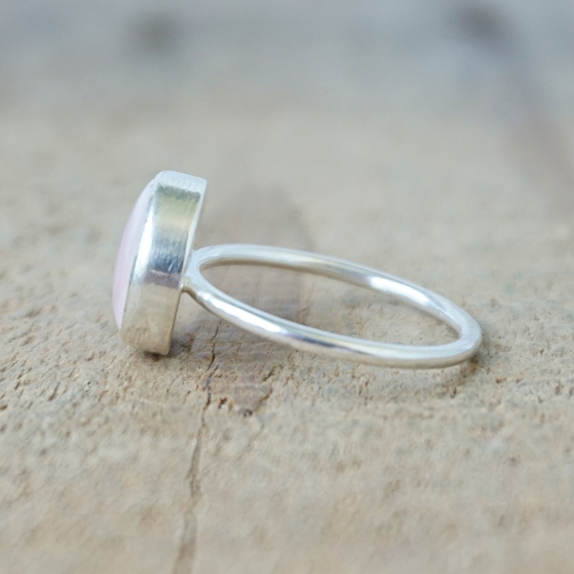 side view of a silver ring with a light pink stone on a wooden background