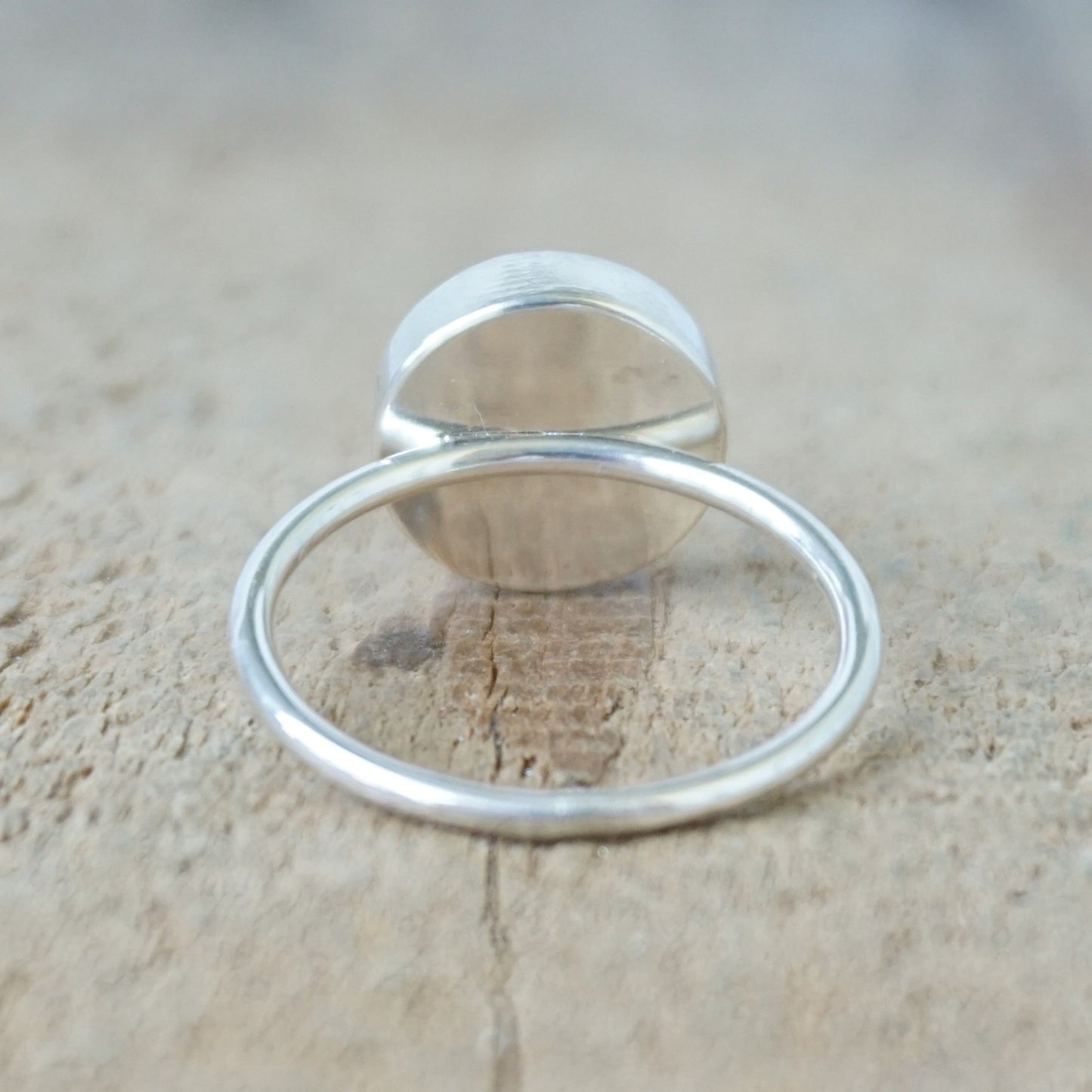back view of a silver ring with a light pink stone on a wooden background