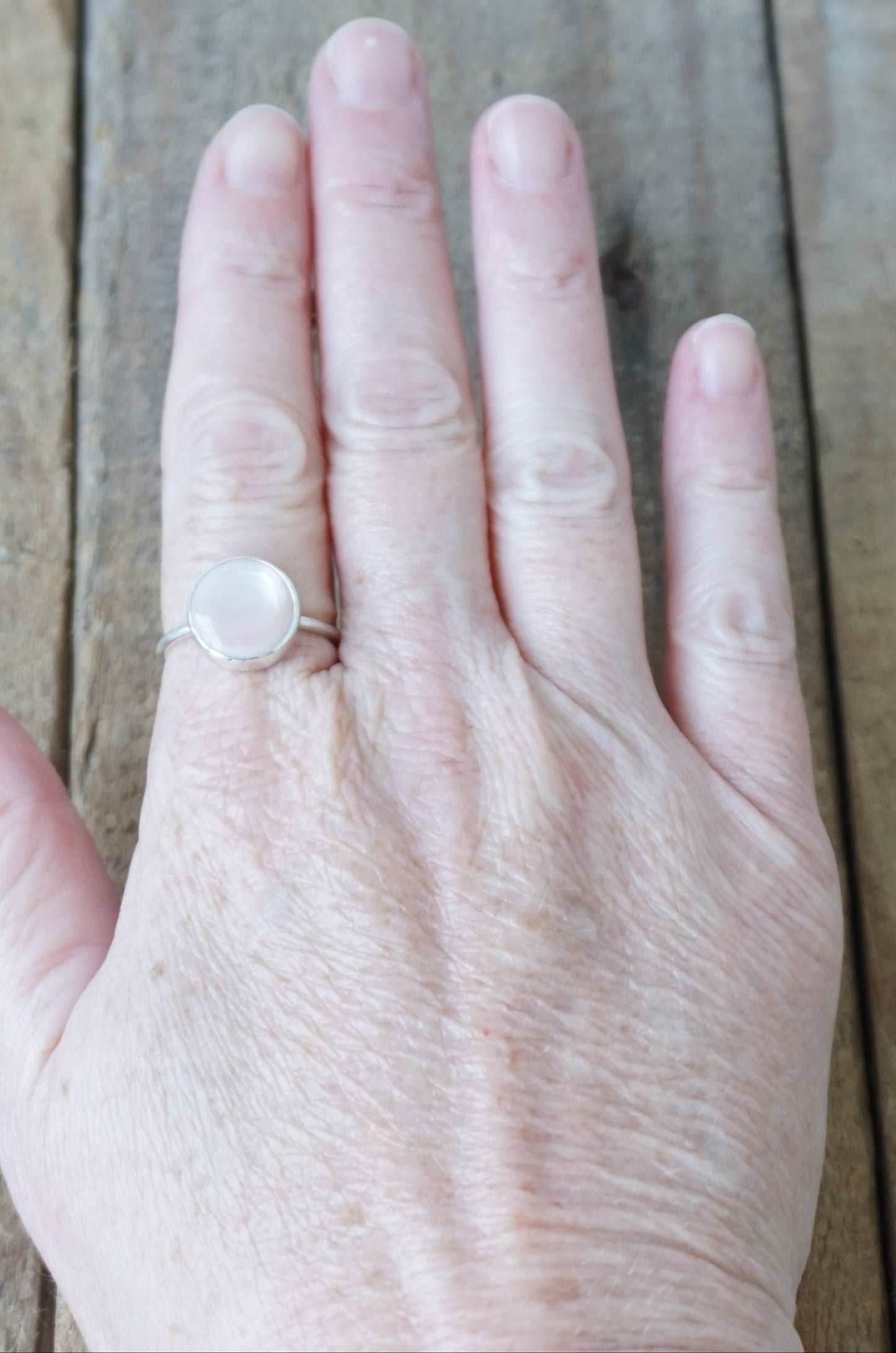 hand wearing a silver ring with a light pink stone on a wooden background