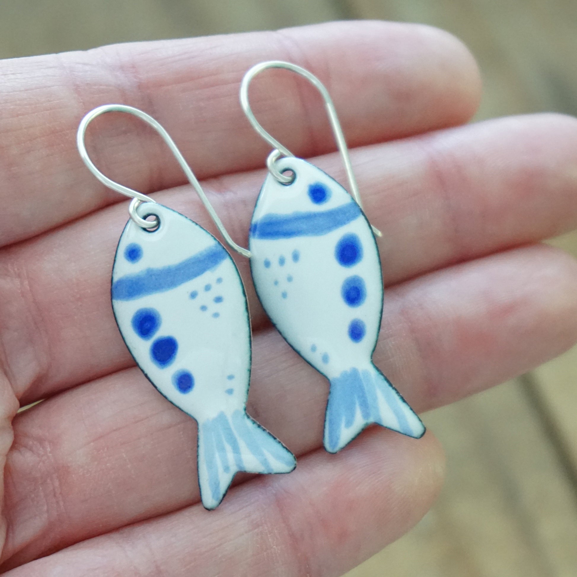 Fish-shaped earrings with blue and white design held in a hand.
