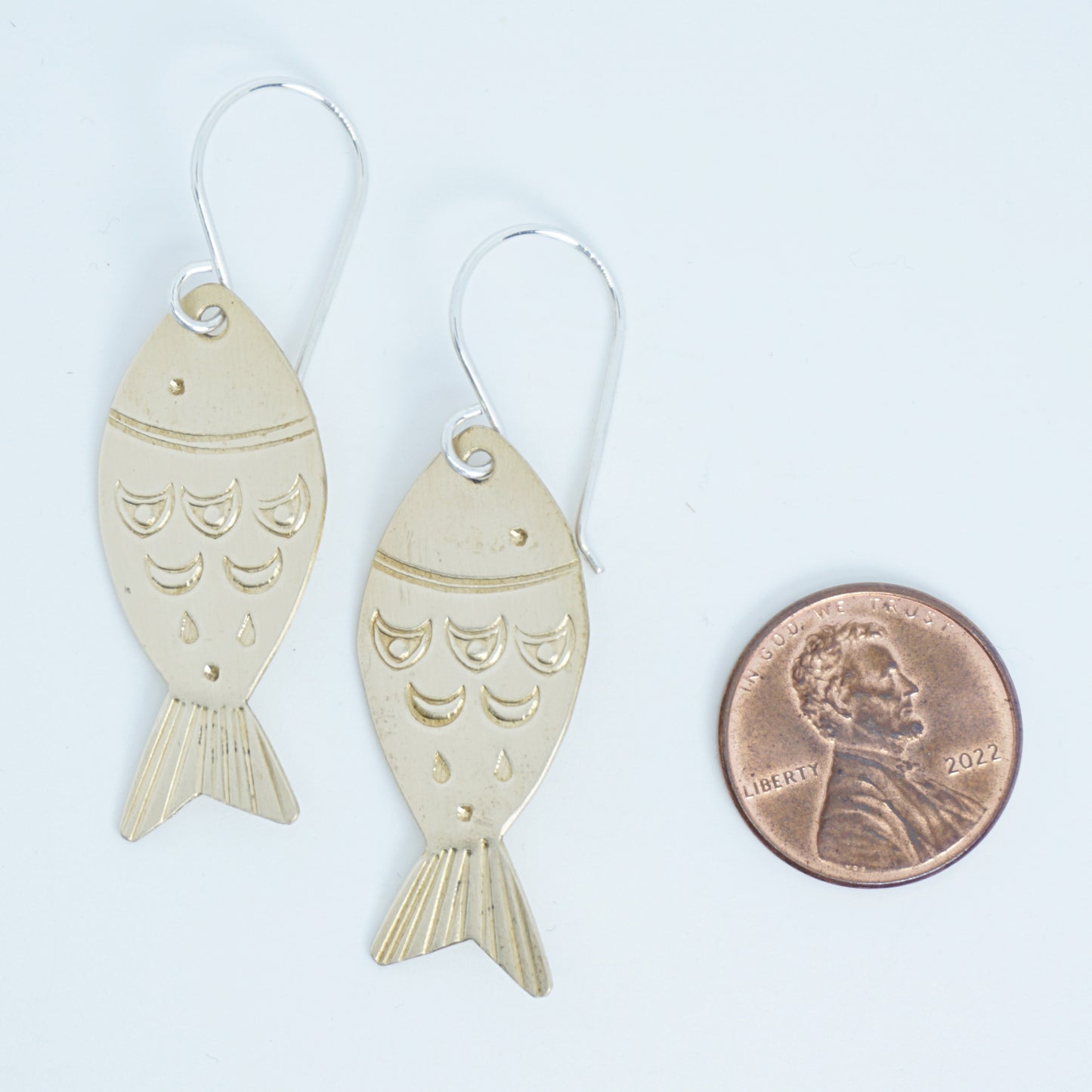 Gold fish-shaped earrings next to a penny for size comparison on a white background