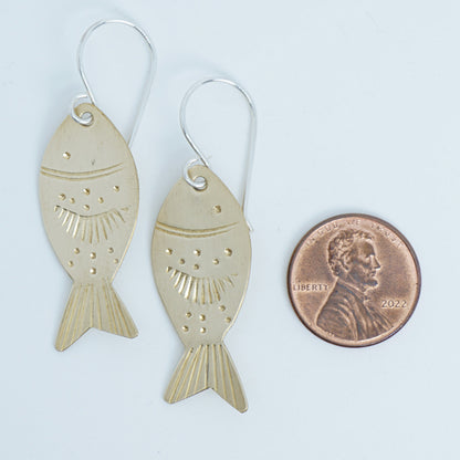 Gold fish-shaped earrings next to a penny for scale on a white background