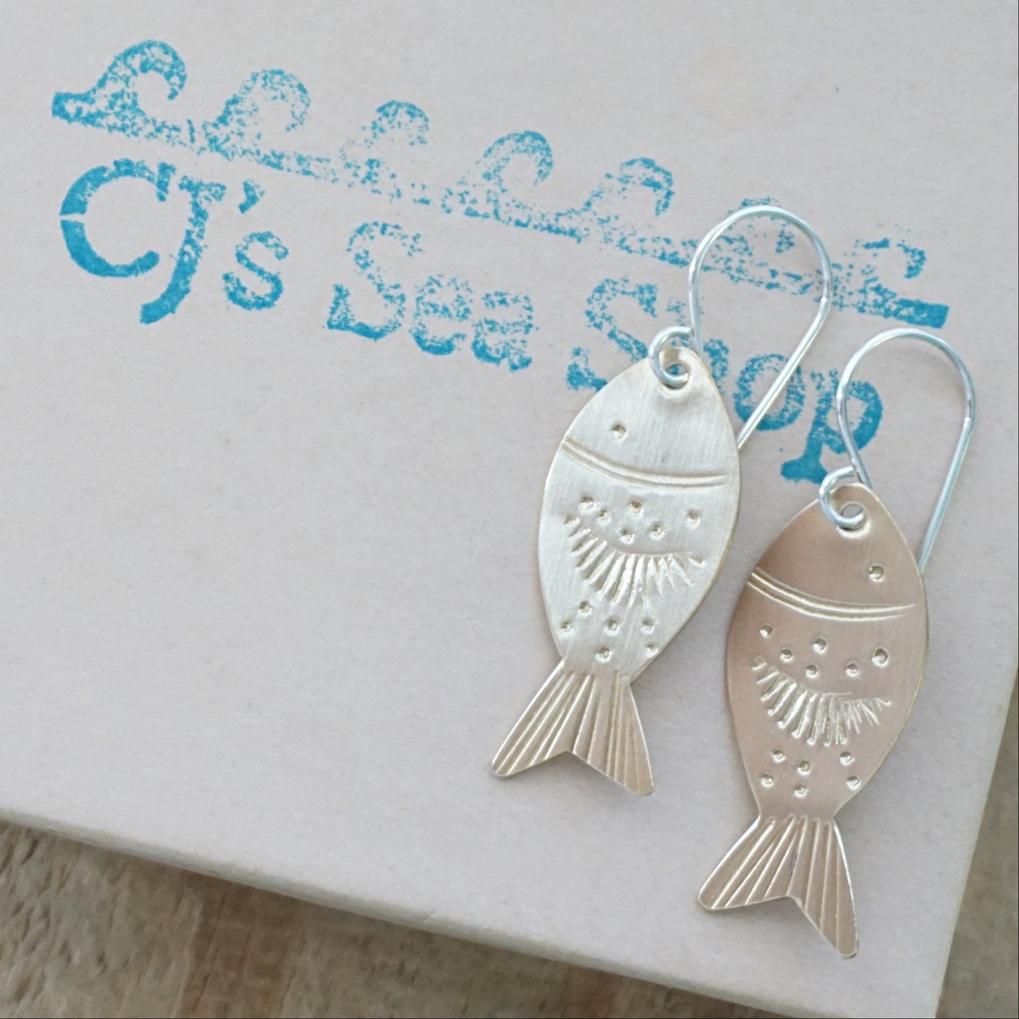 Gold fish-shaped earrings on a gift box.