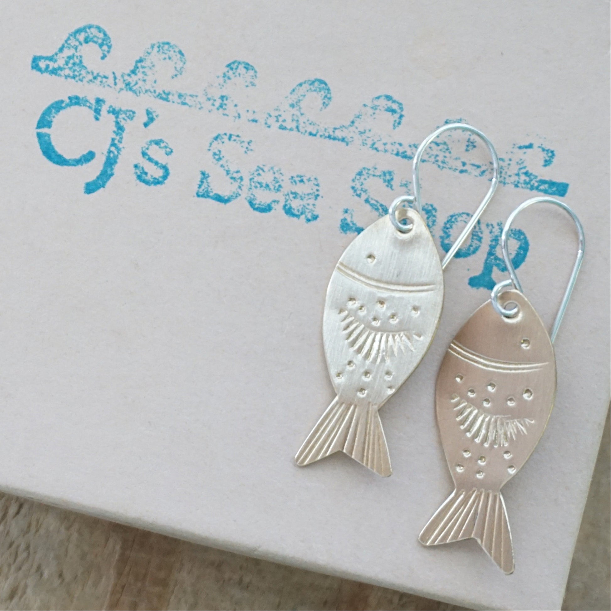 Gold fish-shaped earrings on a gift box.