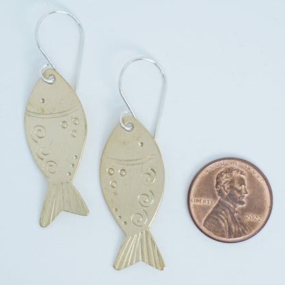 Fish-shaped earrings next to a penny for size comparison on a white background