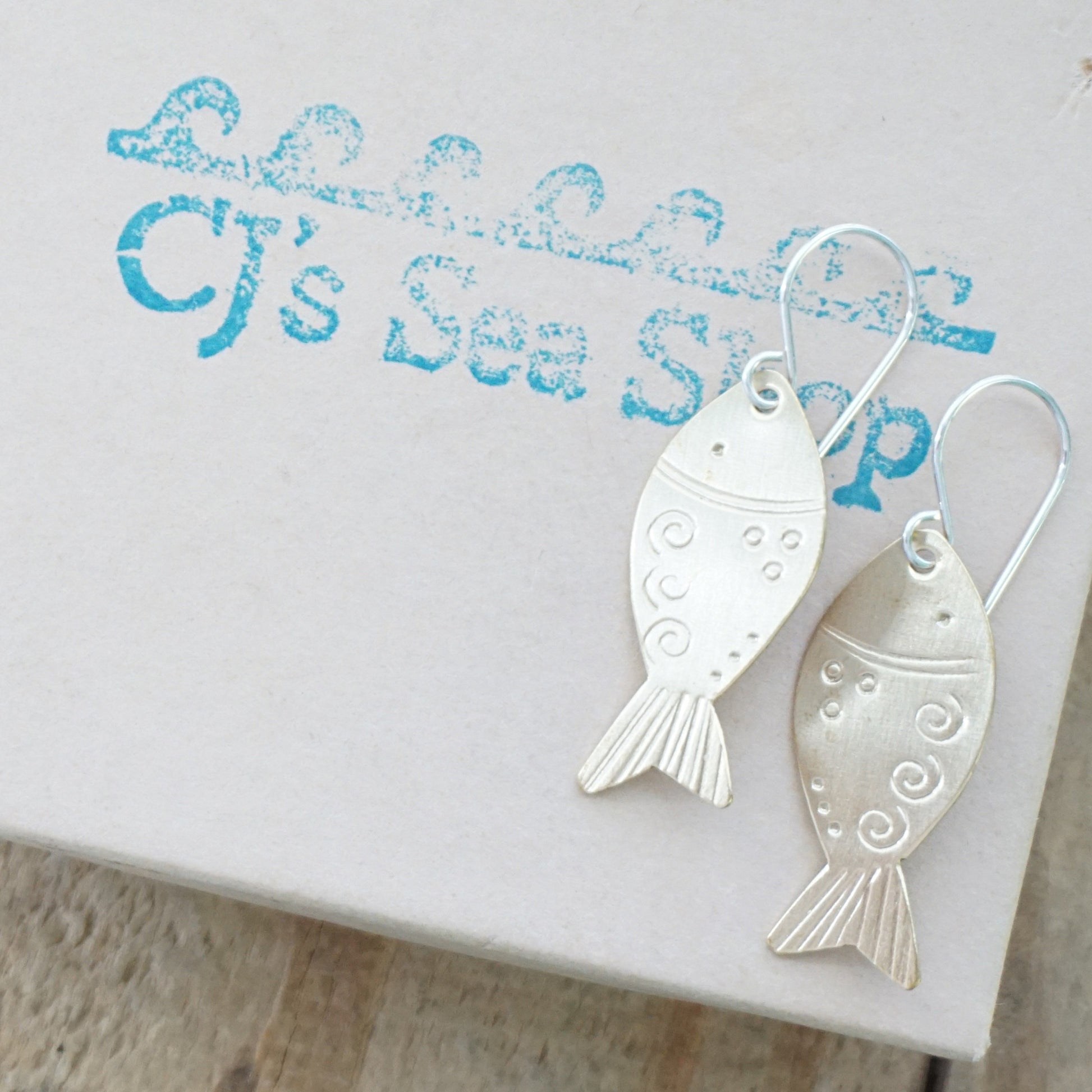 Brass fish-shaped earrings on a gift box